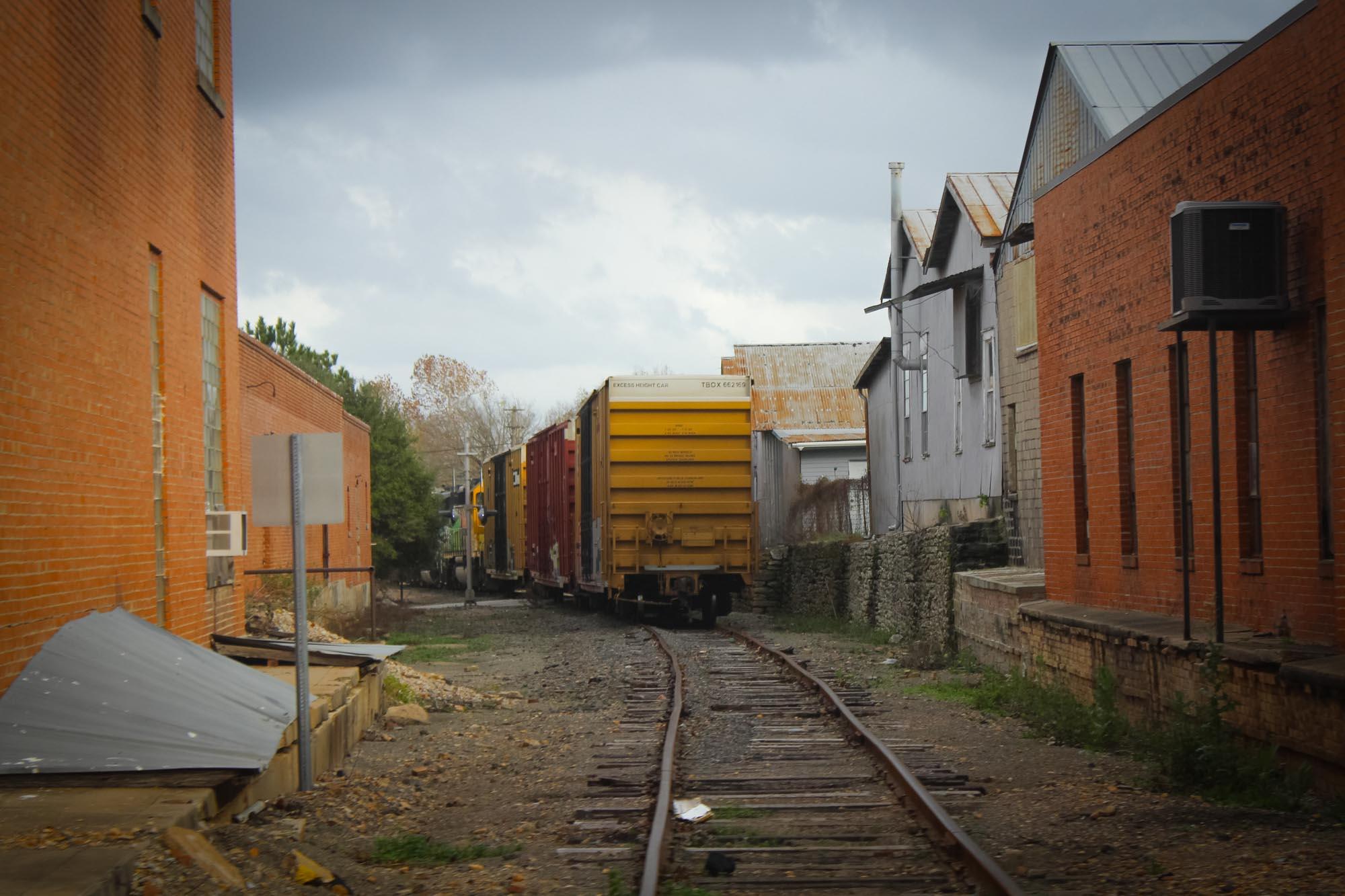 A train consisting of three box cars traveling away on railroad tracks between buildings